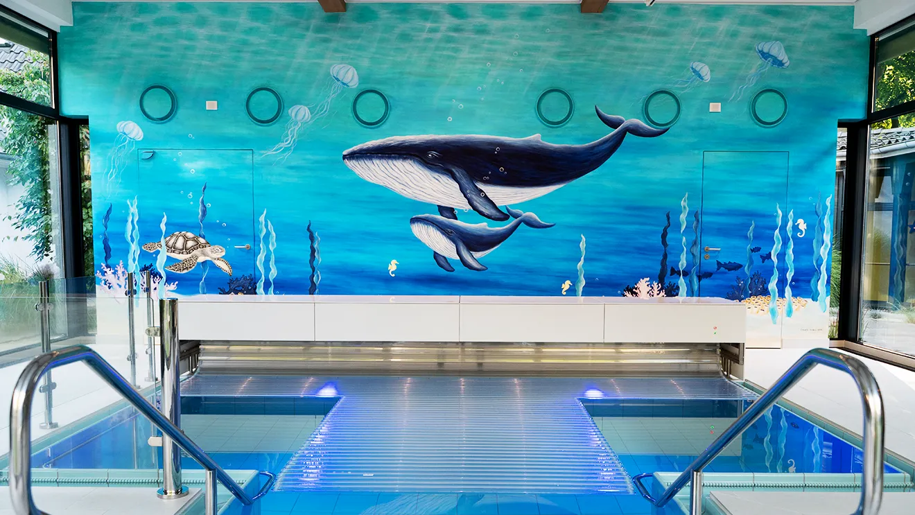 Innenpool mit einem farbenfrohen Wandgemälde, das Wale und eine Meeresschildkröte zeigt, umgeben von Glaswänden und Edelstahlgeländern.