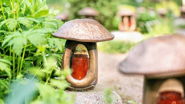 Pilzförmige Gartenleuchten mit bernsteinfarbenem Glas, umgeben von üppigem Grün und auf einem Steinweg platziert.
