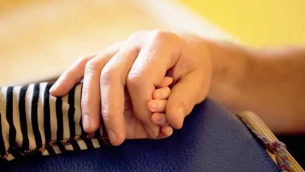 An adult's hand holds the hand of a small child.