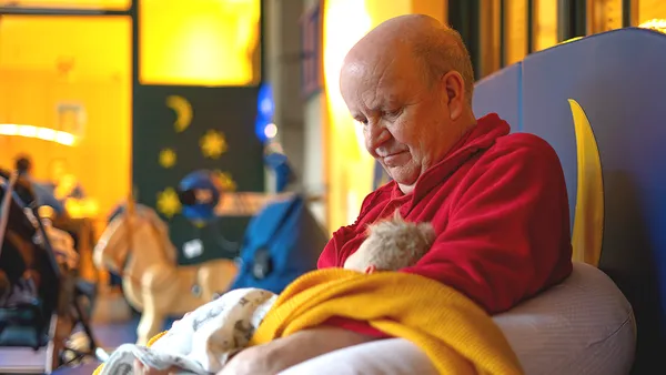 Ein Mann in roter Fleecejacke hält einen kleinen Jungen in seinen Armen und blickt sanft auf ihn herab.