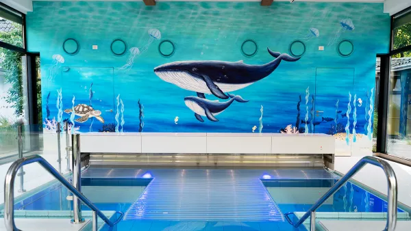 Innenpool mit einem farbenfrohen Wandgemälde, das Wale und eine Meeresschildkröte zeigt, umgeben von Glaswänden und Edelstahlgeländern.