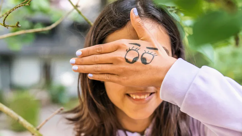 Ein Mädchen verdeckt ihre Augen mit der Hand. Auf der Hand sind Augen aufgezeichnet.