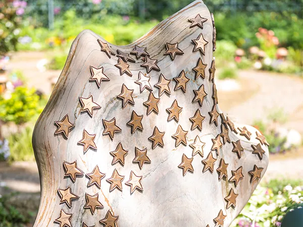 Stone sculpture adorned with carved stars, set in a garden with blurred greenery and pathways in the background.