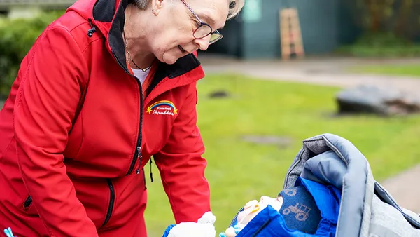 Eine ältere Frau in roter Jacke blickt liebevoll auf einen kleinen Jungen im Kinderwagen. Er trägt Winterkleidung.