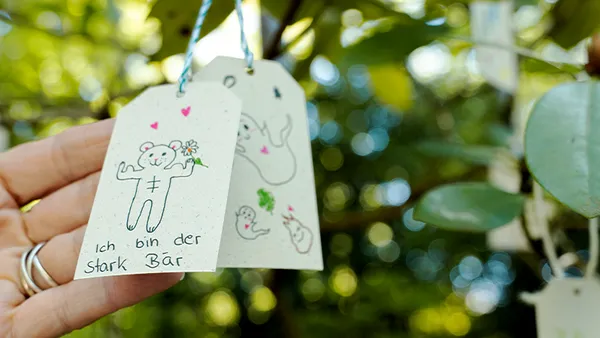 Hand, die ein Schild mit einer Zeichnung eines Bären und dem deutschen Text „Ich bin der Stark Bär“ vor einem verschwommenen Hintergrund aus Grün hält.