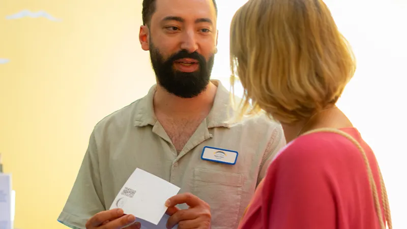 Vier Frauen in blauer Arbeitskleidung diskutieren in einem hell erleuchteten Raum mit Informationsdisplays und Pflanzen über ein Buch.